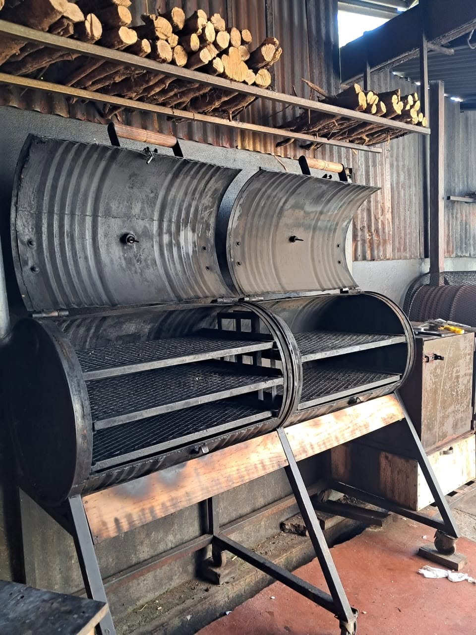 Parrillas para BBQ tipo barril junto a una reserva de leña